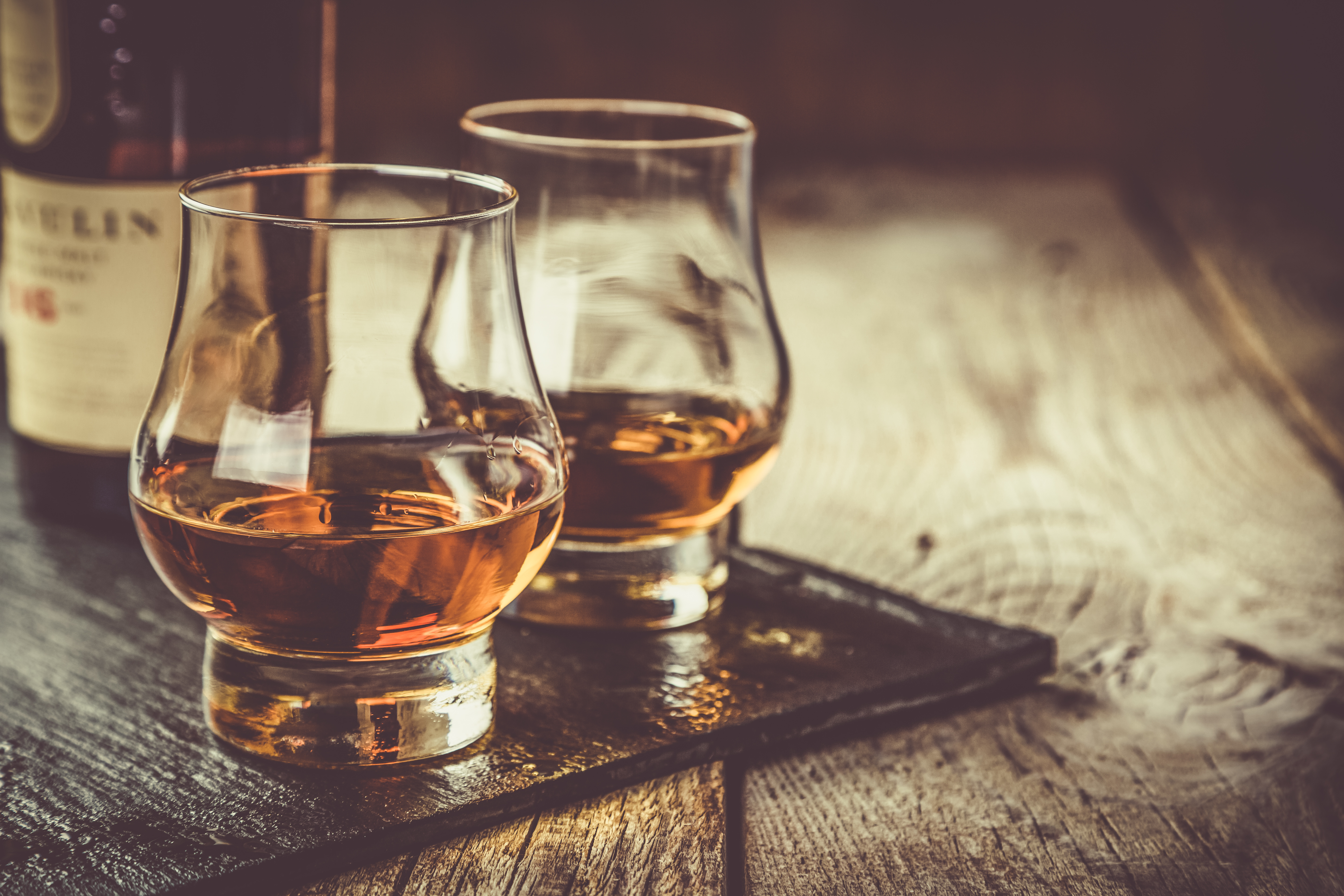 Whiskey with ice in glasses, rustic wood background, copy space