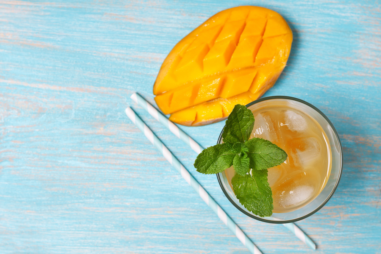 Alcoholic mango ice tea with mint in a glass on blue wooden background.
