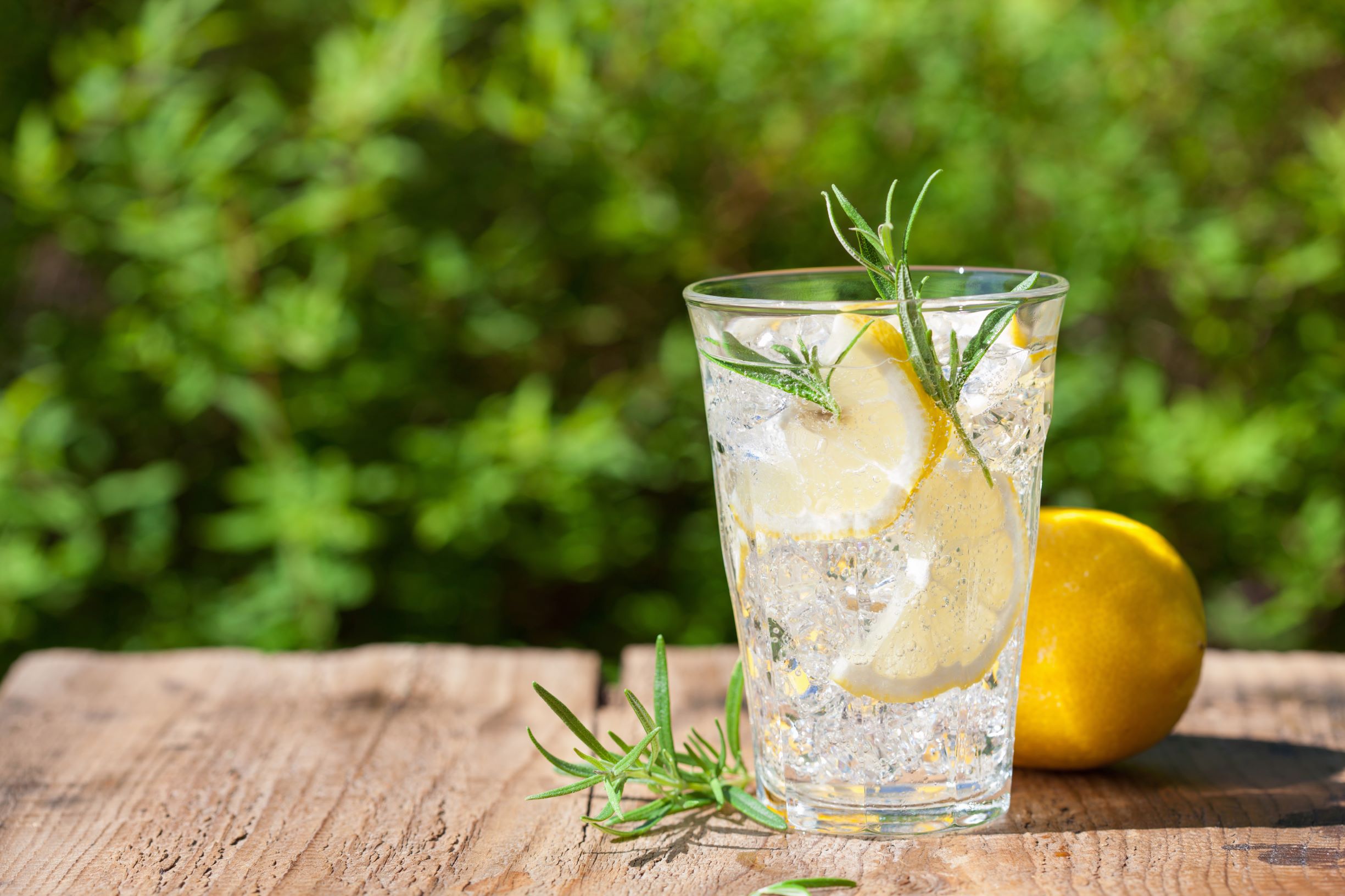 Refreshing lemon drink with herbs and a lemon on a wood table outside