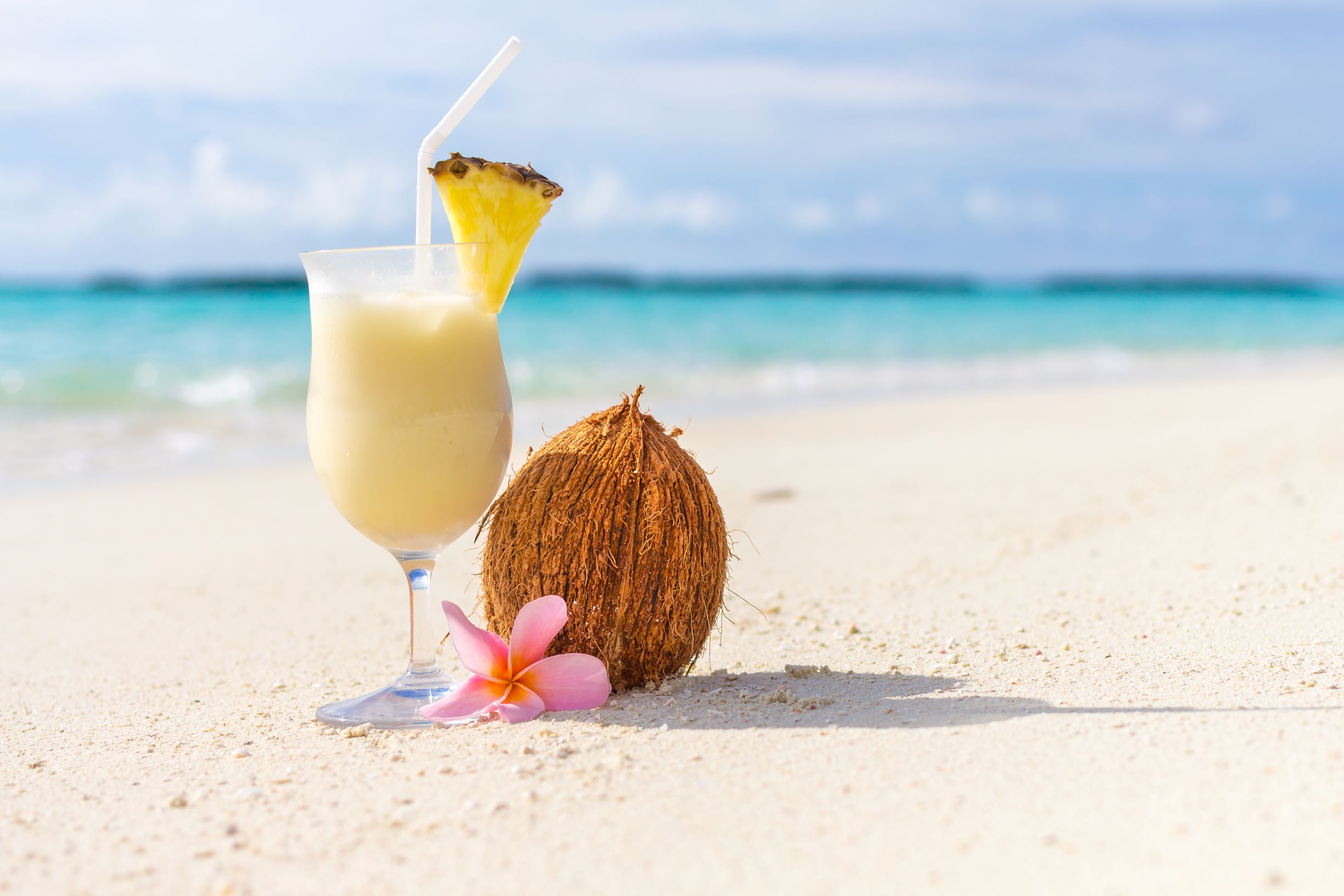 Glass of pina colofa cocktail on a white sandy beach and a coconut