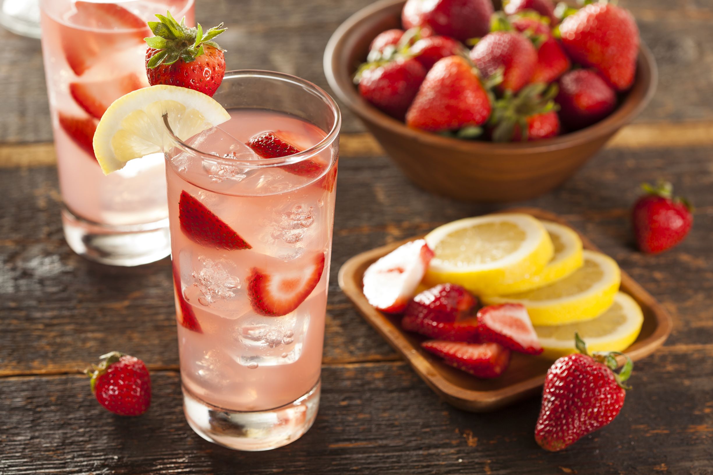 Strawberry Lemonades with strawberry and lemon garnishes and a bowl of strawberries and lemon slices