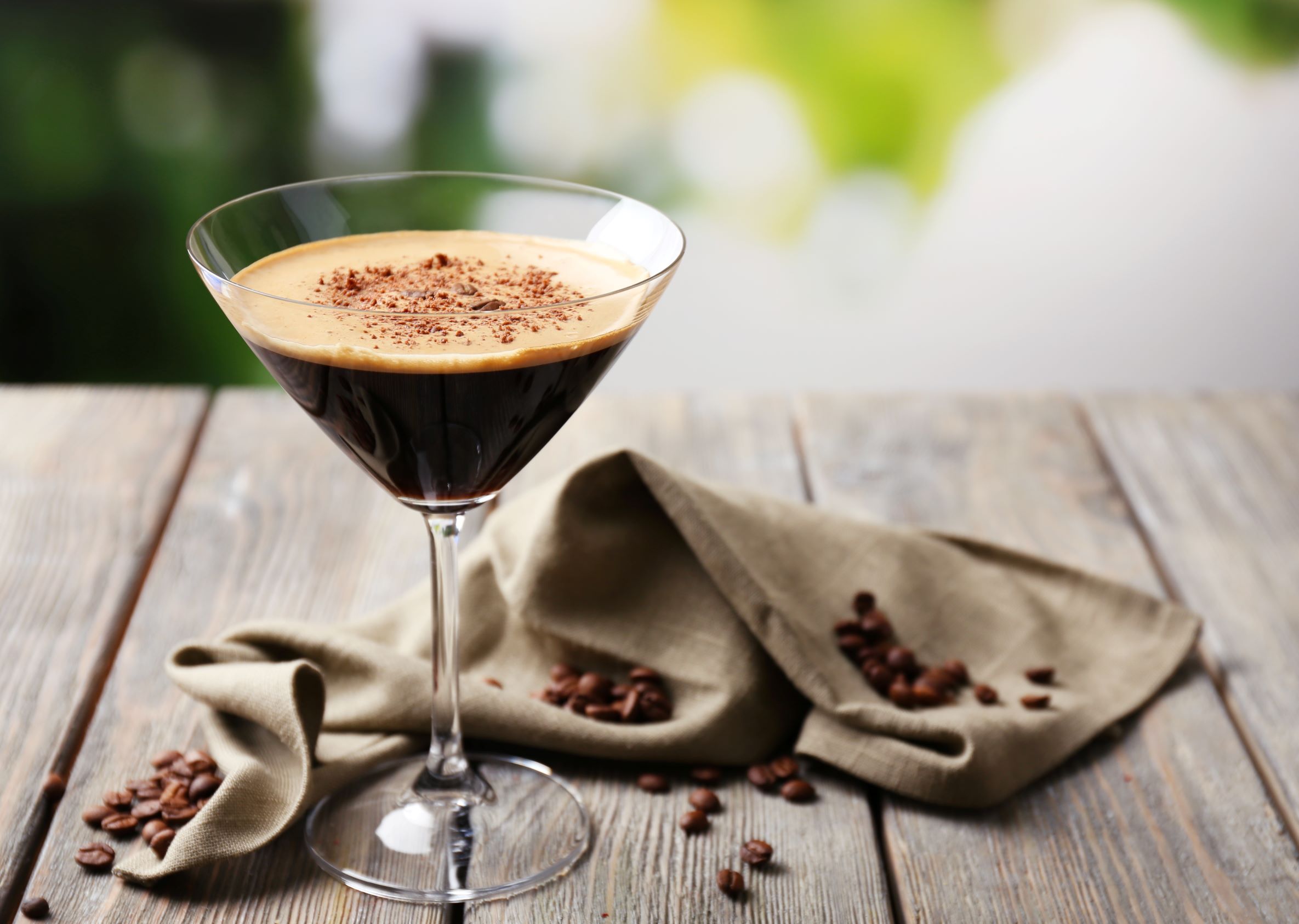 Classy glass of espresso martini on a wooden table with a kitchen cloth and coffee beans