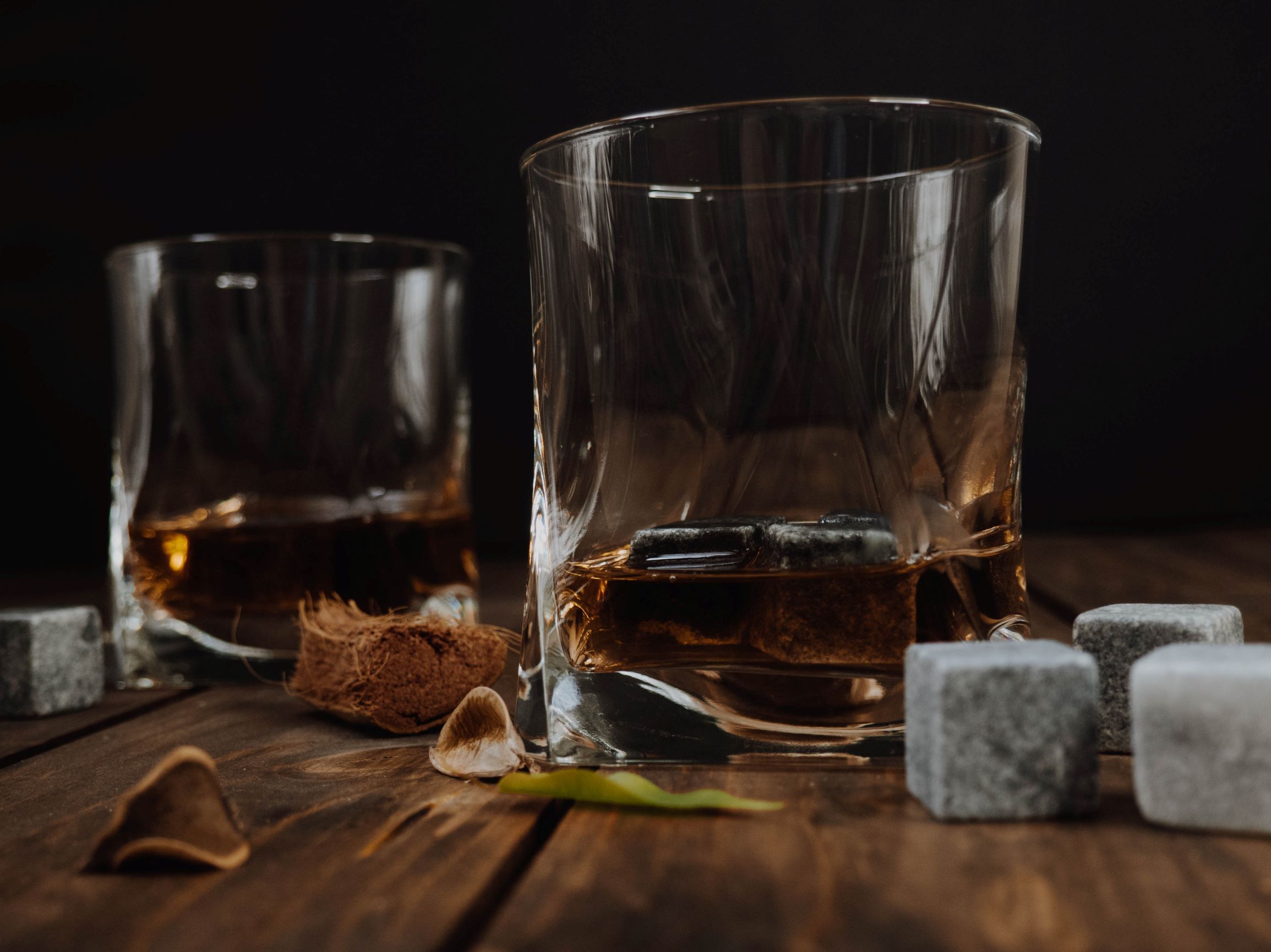 Two whiskey glasses on a wooden table with various aromatics and a dark background