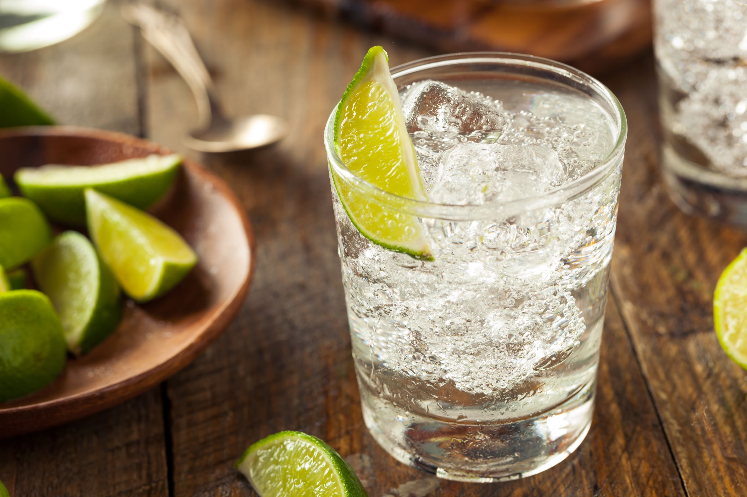 Clear glass of a vodka soda with lime wedges on a wooden table