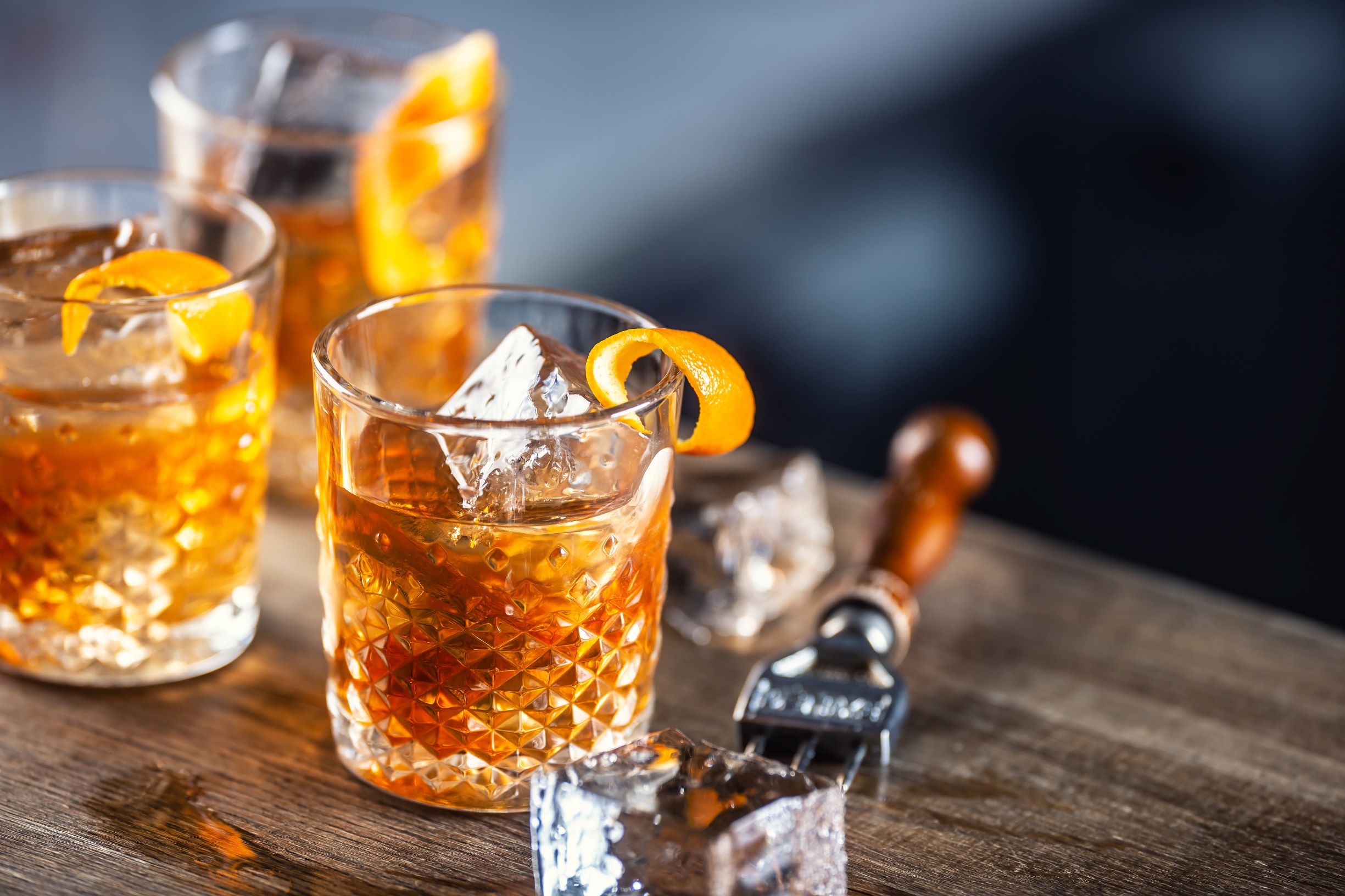 Three old fashioned whiskies with orange peel garnishes.