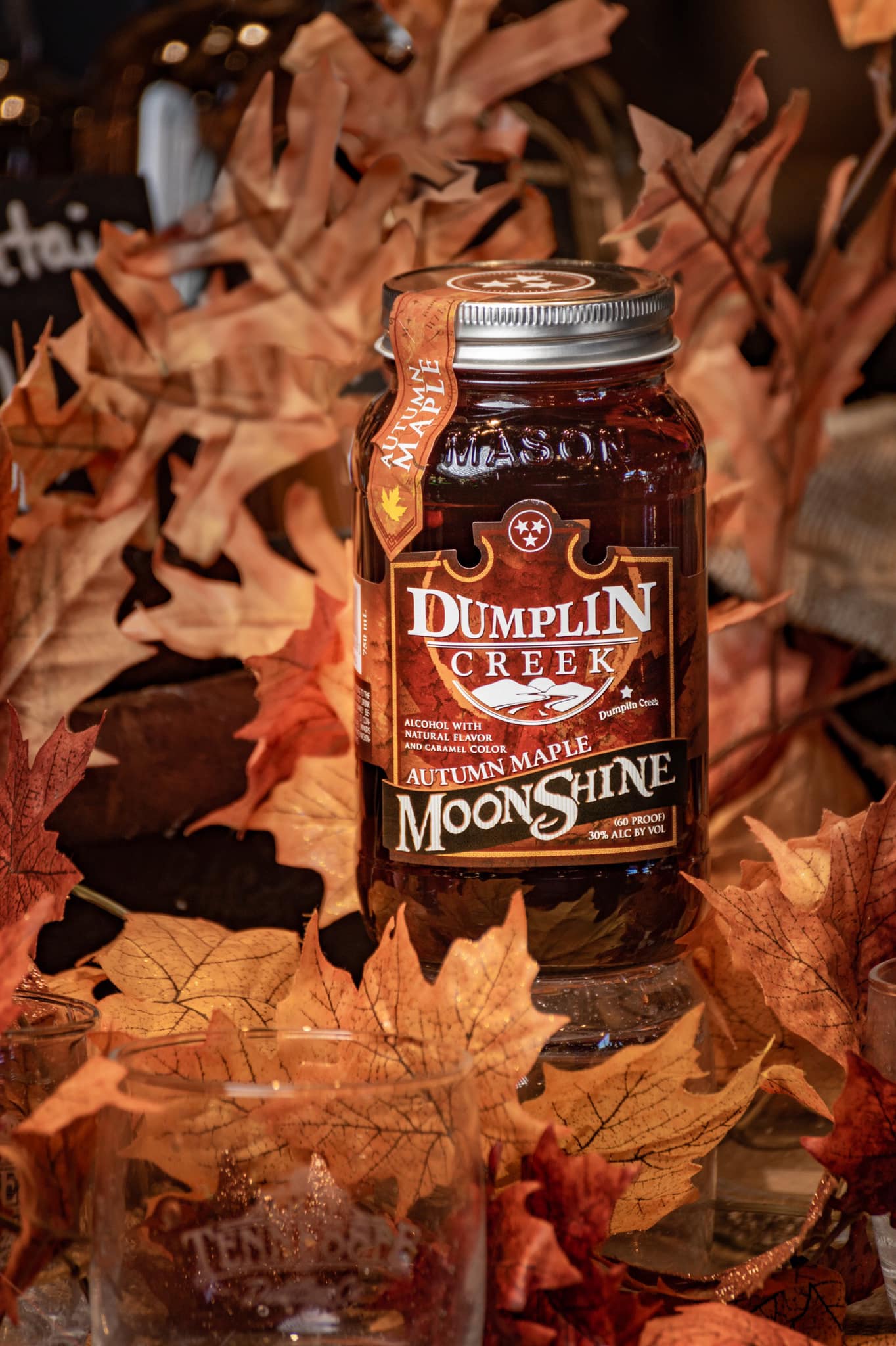 Jar of Dumplin Creek Autumn Maple Moonshine with fall leaves in the background.