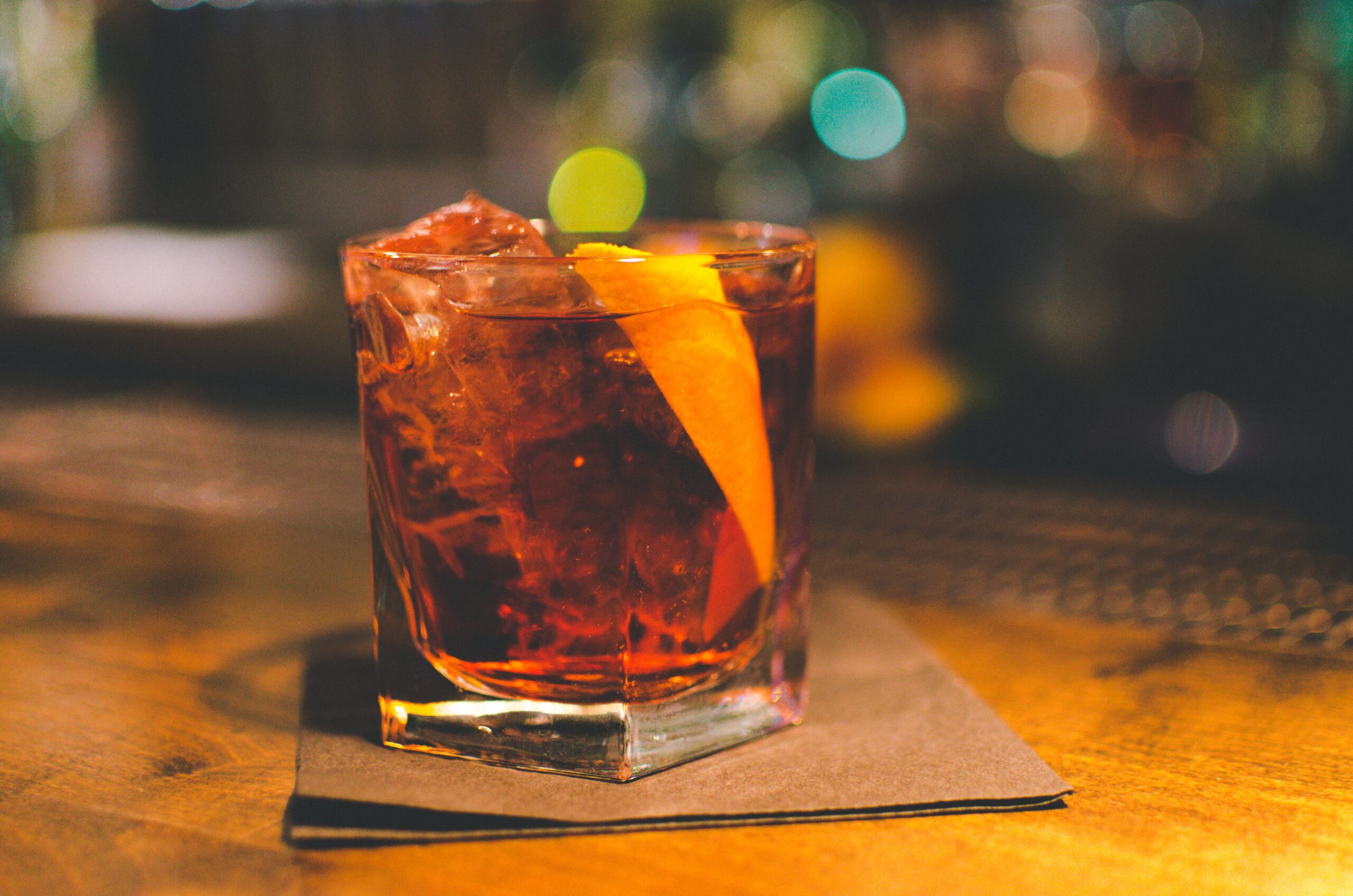 A cocktail on a bar with an orange peel garnish.