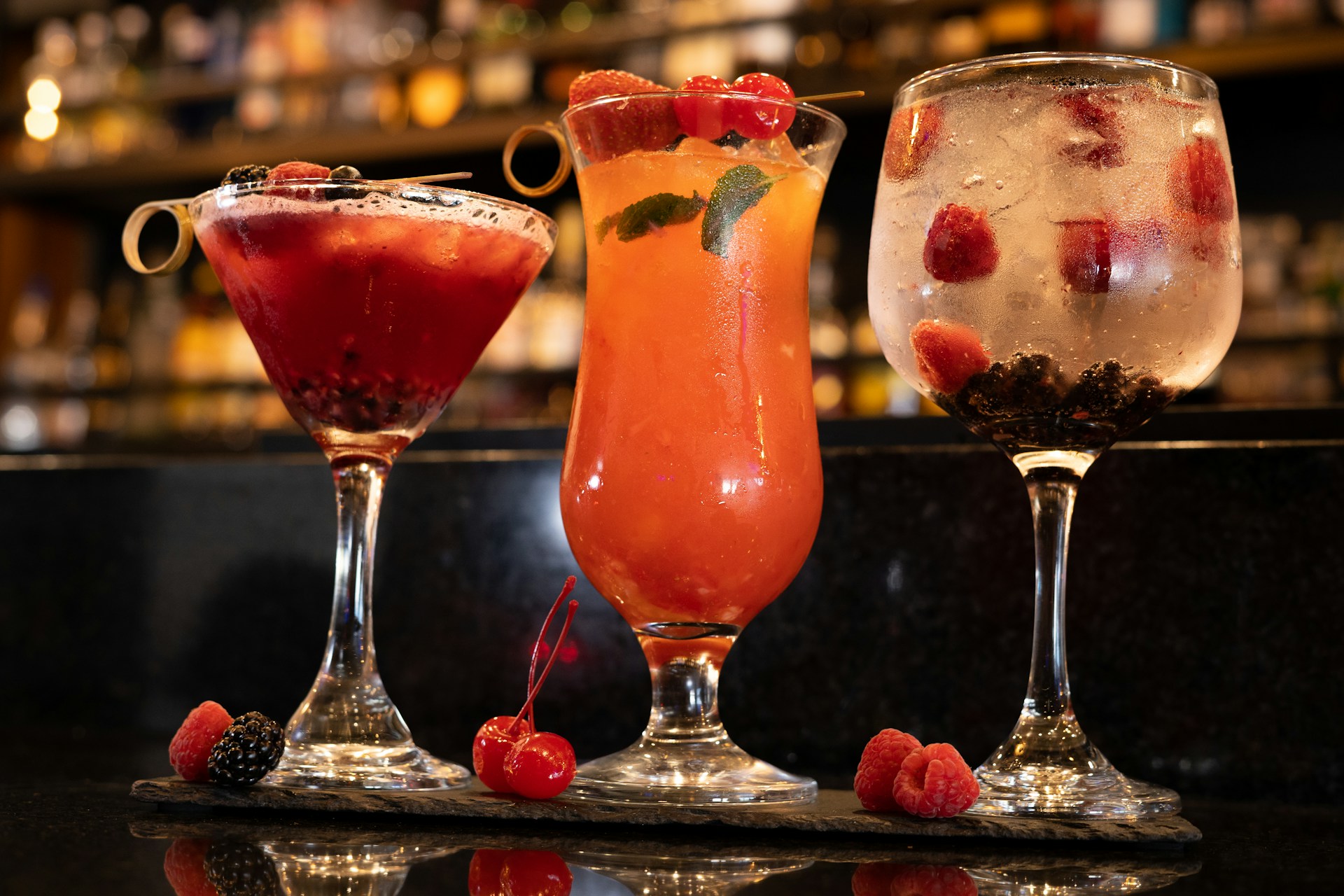 Three different cocktails on a bar featuring moonshine cherries