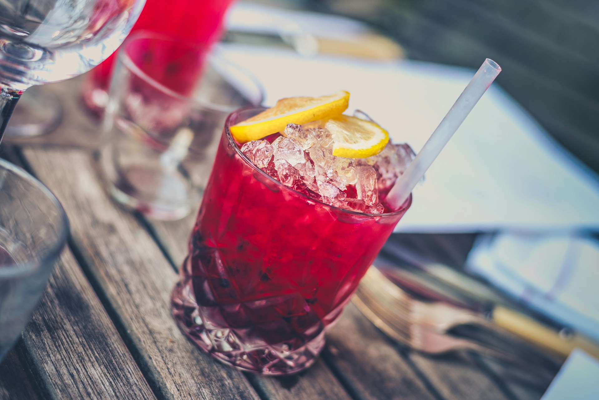 A glass tumbler containing a purple cocktail and lemon slices as garnish